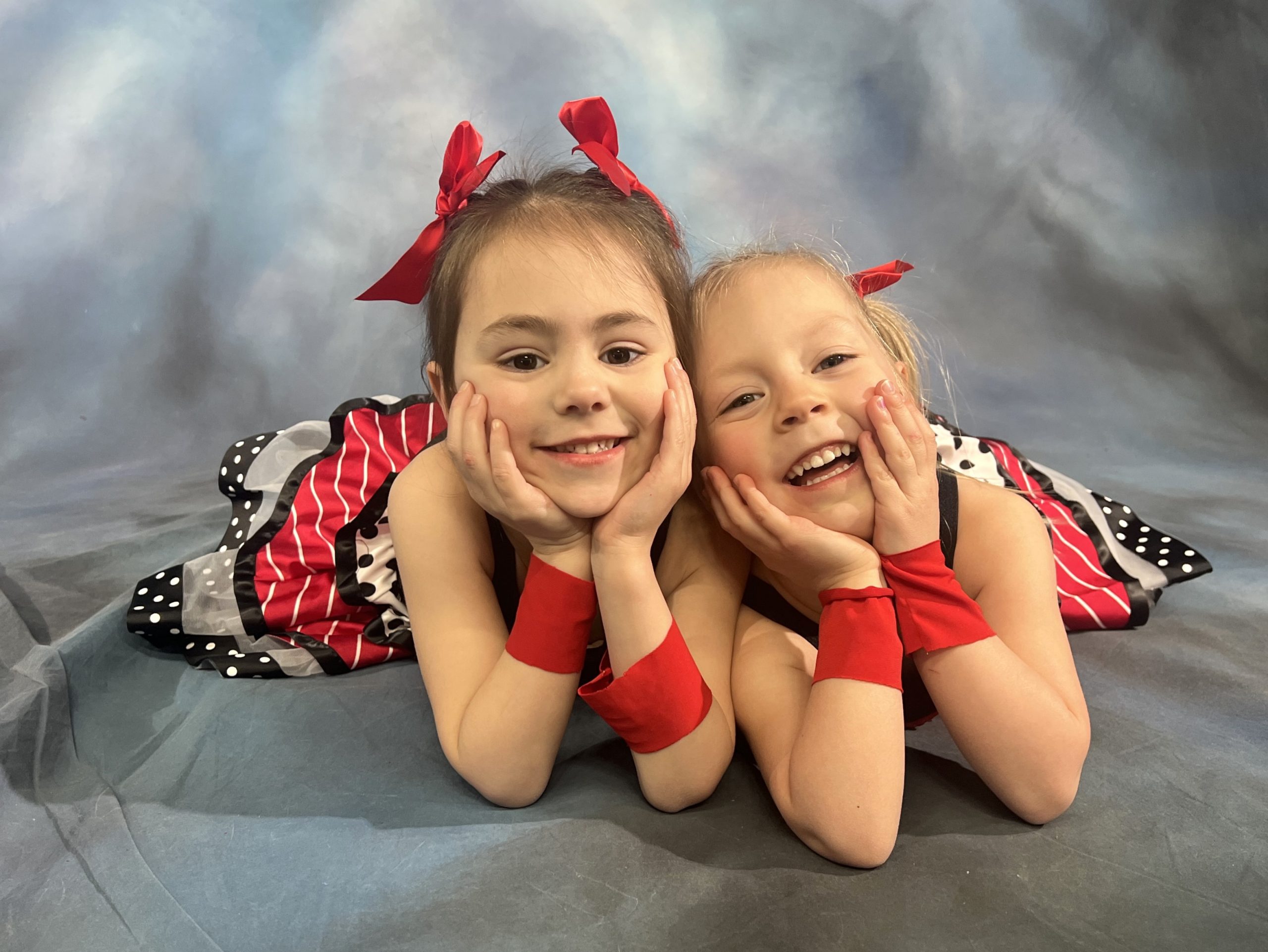 Two girls in red and polka dot tutus lying on ground